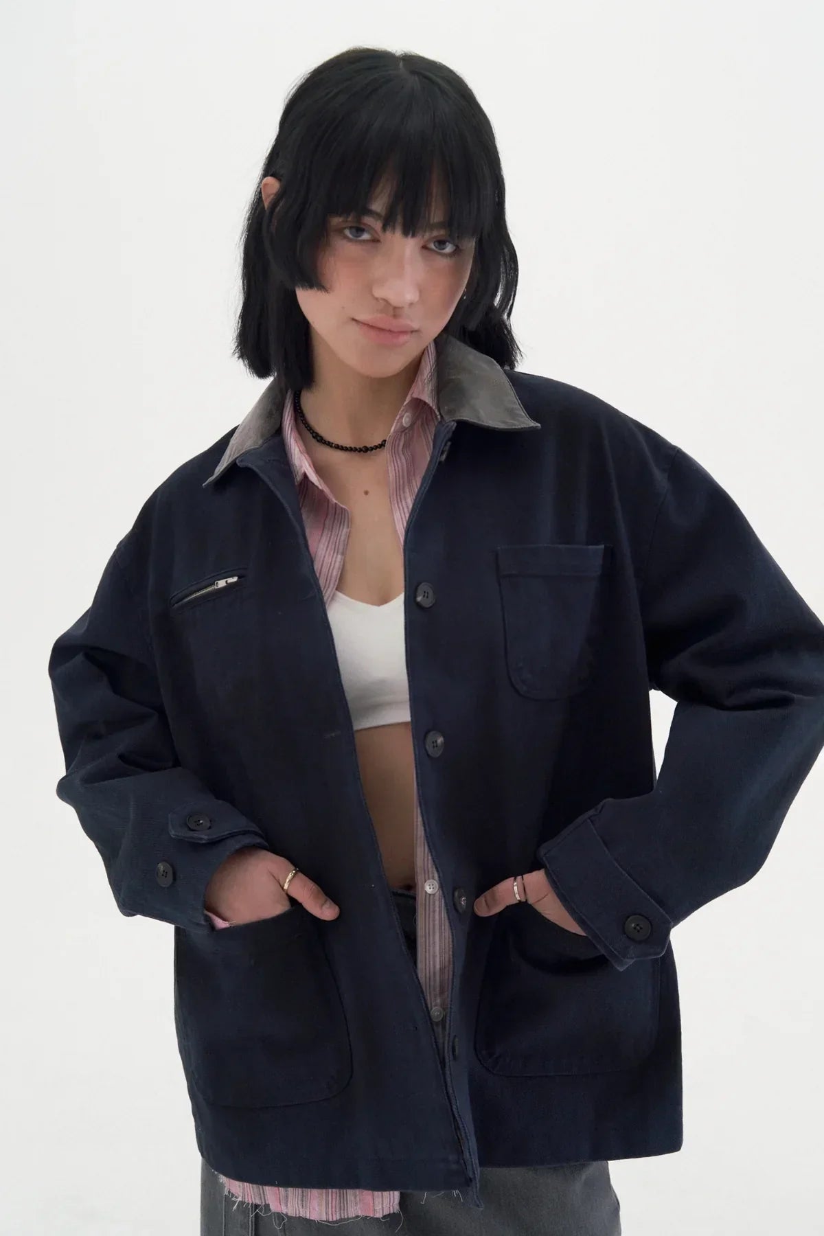 Woman wearing vintage navy work jacket with gray collar over pink striped shirt and white crop top