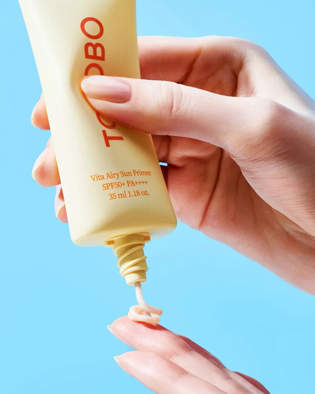 Hand dispensing TOSOBO Vita Airy Sun Primer SPF50+ PA++++ 35ml on finger against blue background