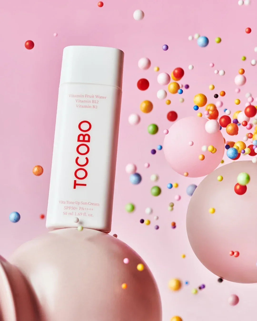 TOCOBO Vita Tone Up Sun Cream SPF50 PA++++ on pink background with colorful floating spheres