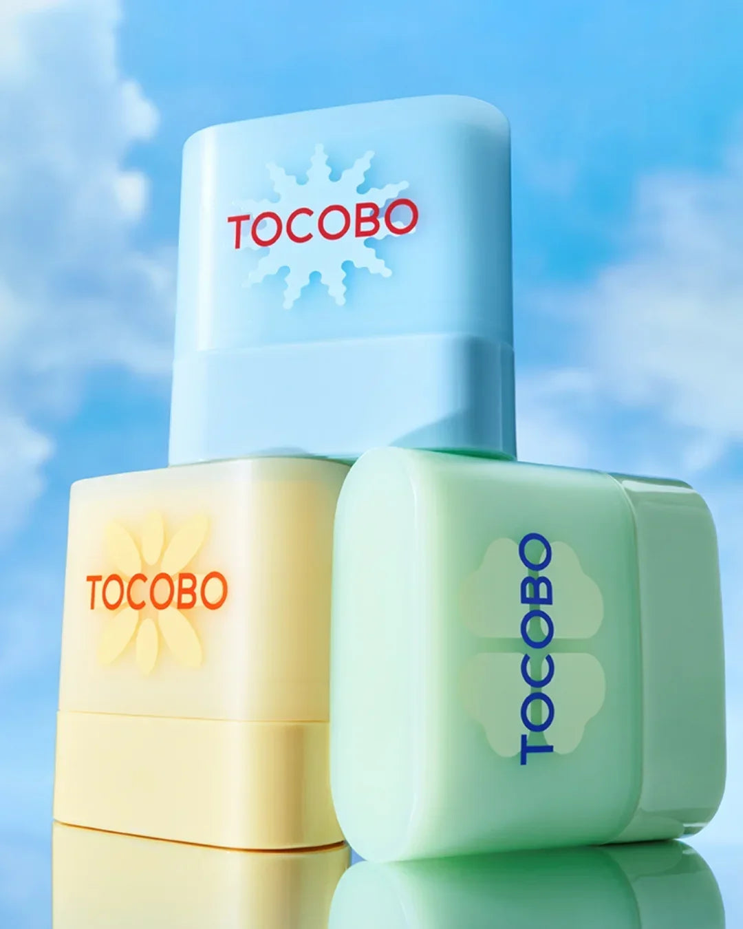 Three pastel-colored TOCOBO skincare containers stacked against blue sky background