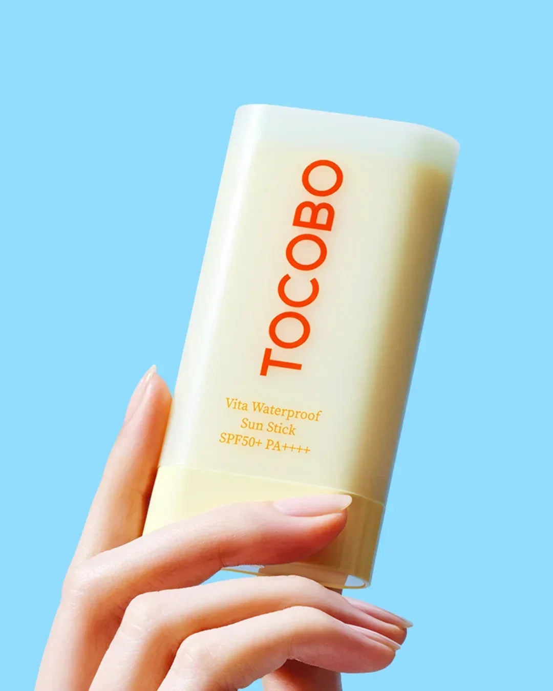 Hand holding Tocobo Vita Waterproof Sun Stick SPF50+ PA++++ with light blue background