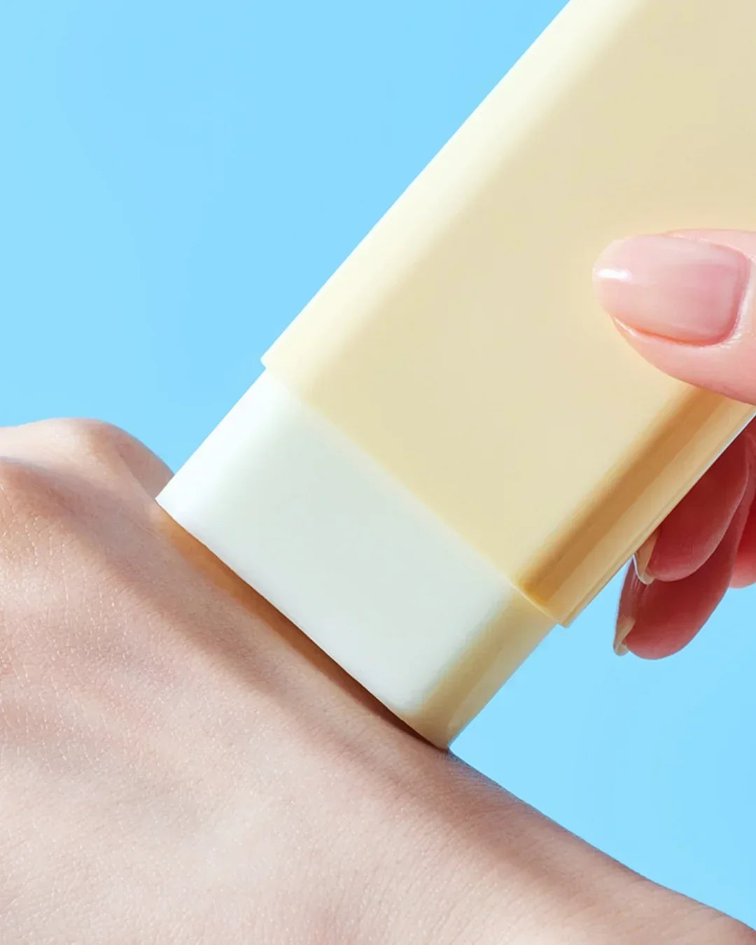 Hand applying yellow waterproof sun stick SPF50 PA++ sunscreen on skin against blue background