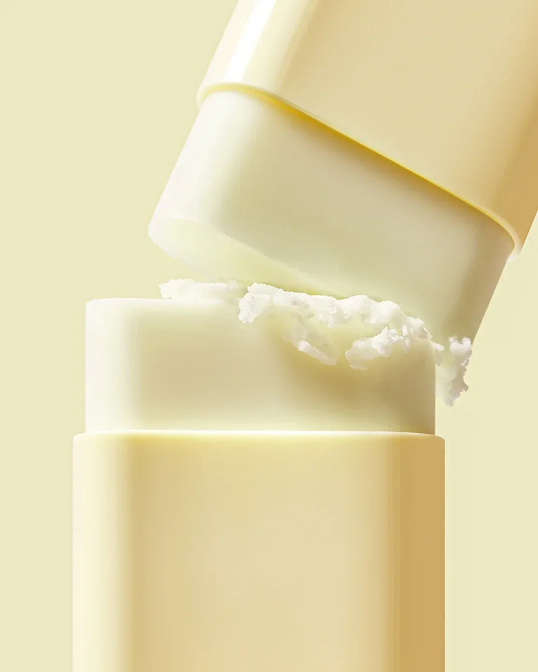 Close-up of white waterproof sun stick SPF50 PA container with creamy texture on light yellow background
