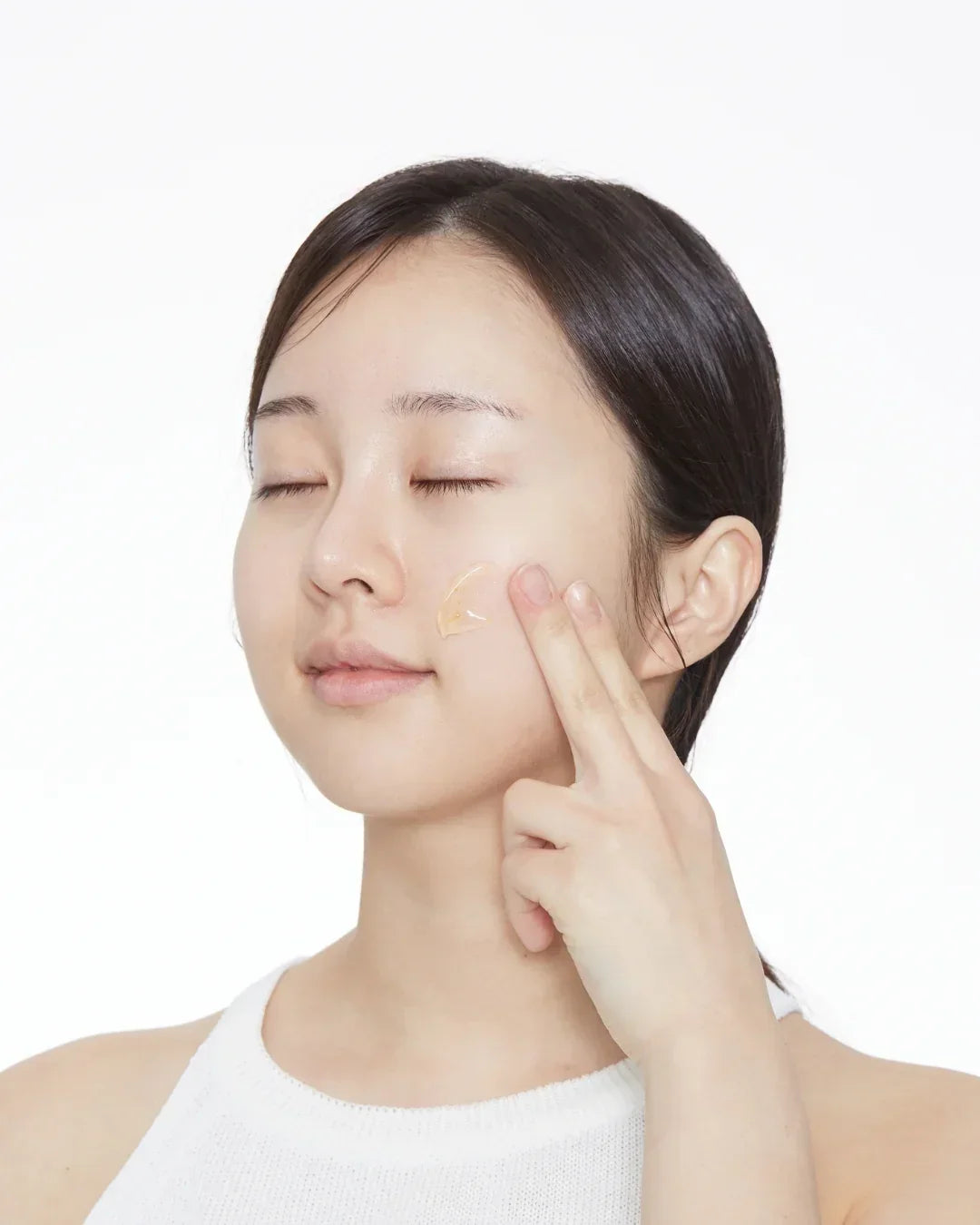 Young woman applying transparent skincare gel on cheek with fingers, natural beauty routine