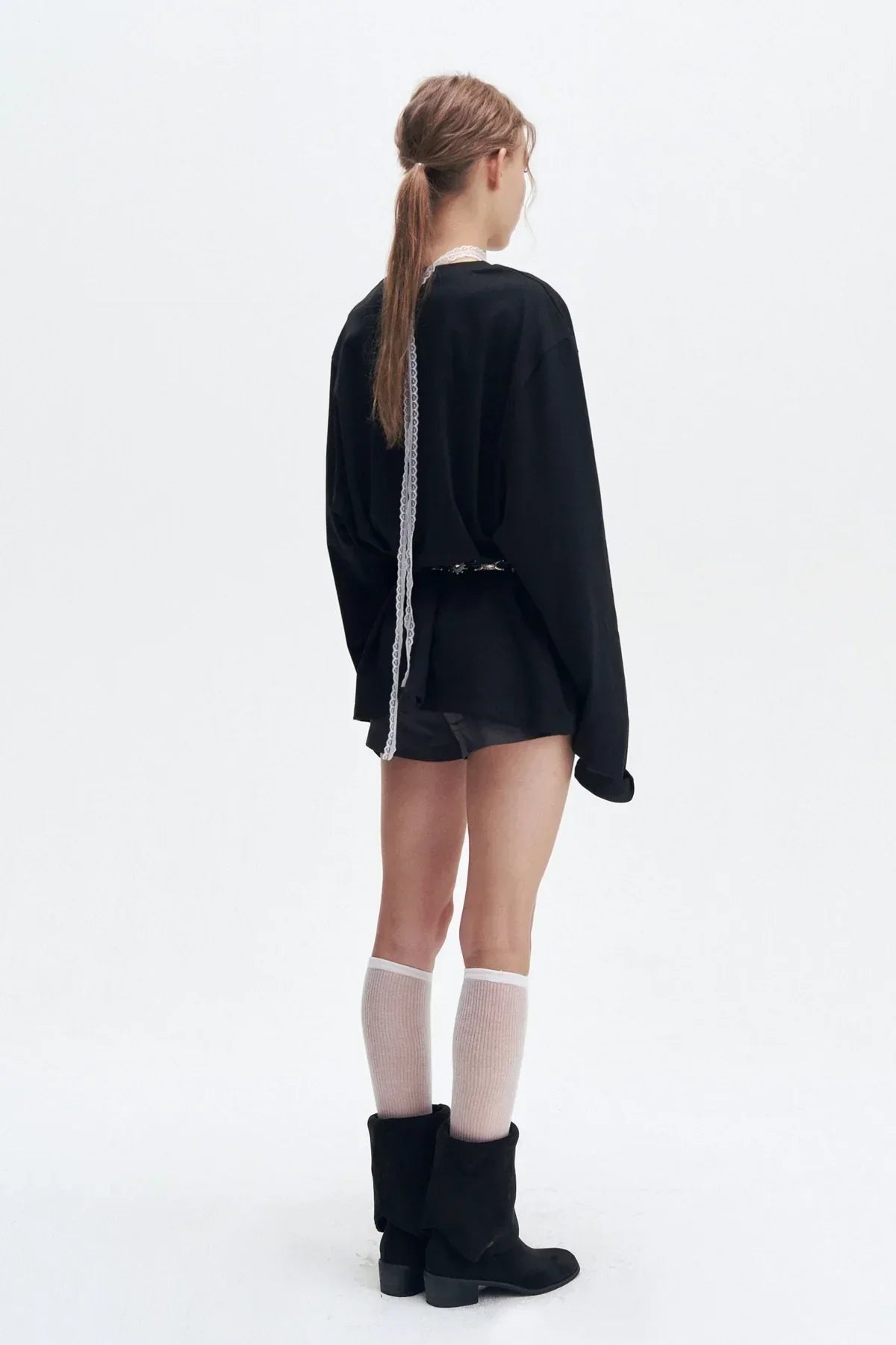 Back view of woman wearing black long sleeve top with white lace detail, black shorts, knee-high white socks, and black boots