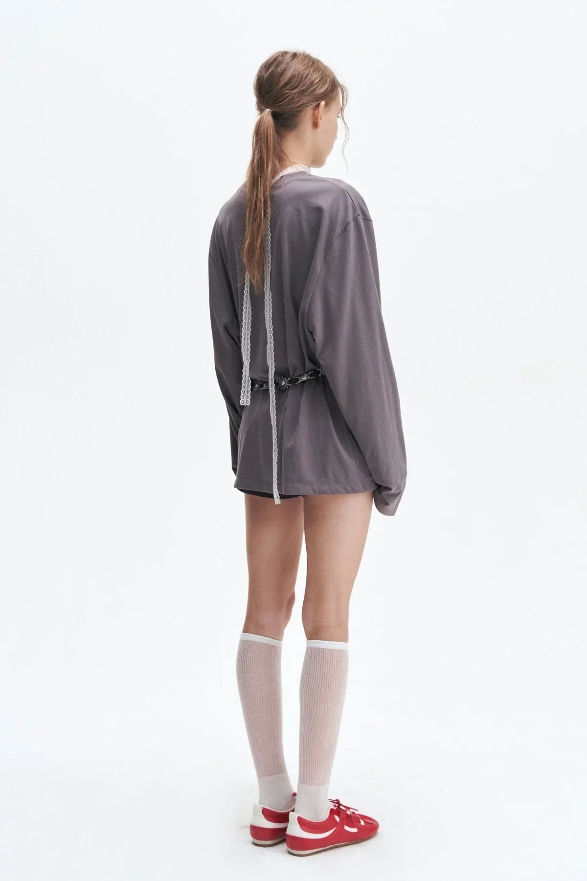 Woman in gray long sleeve shirt, white knee-high socks, and red sneakers against white background