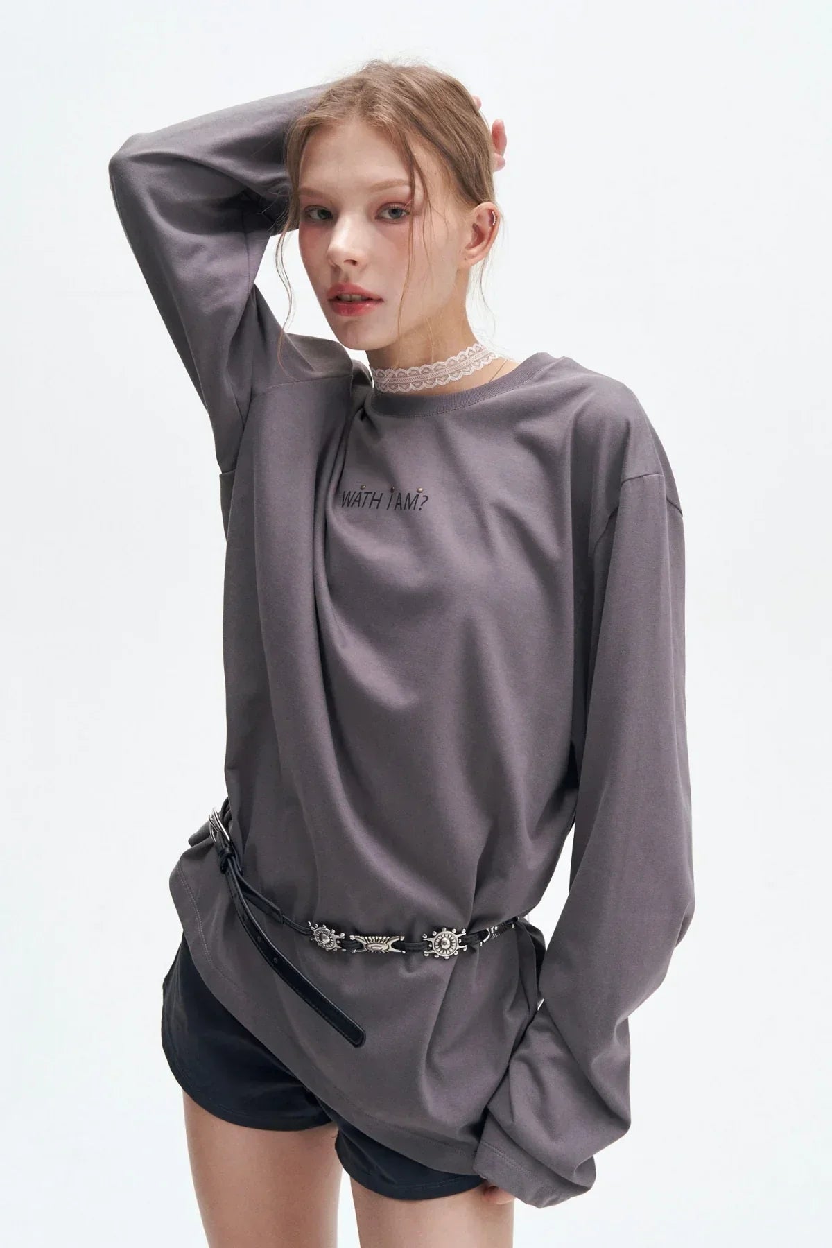 Fashion model wearing oversized gray long sleeve shirt with 'WATH I AM?' text, black shorts, and belt