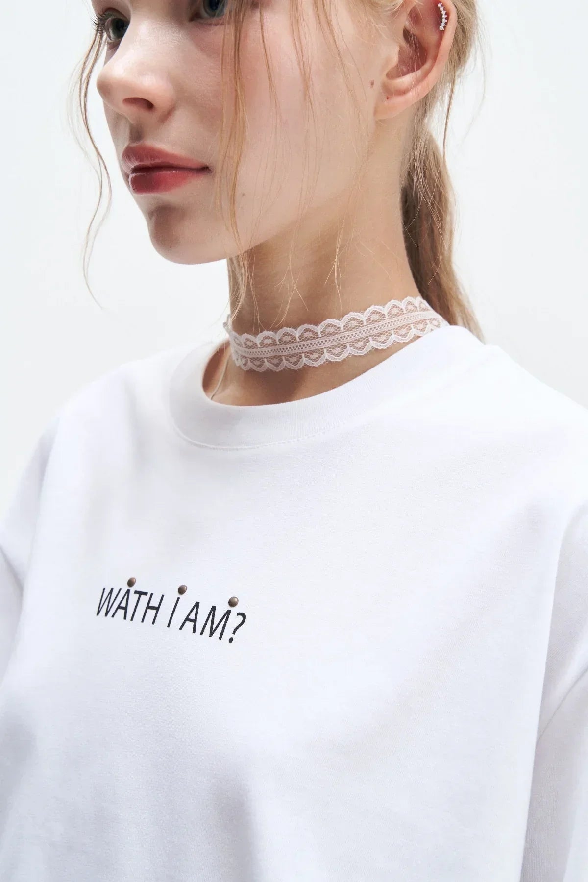 Close-up of woman wearing white sweater with text 'WATH I AM?' and lace choker necklace