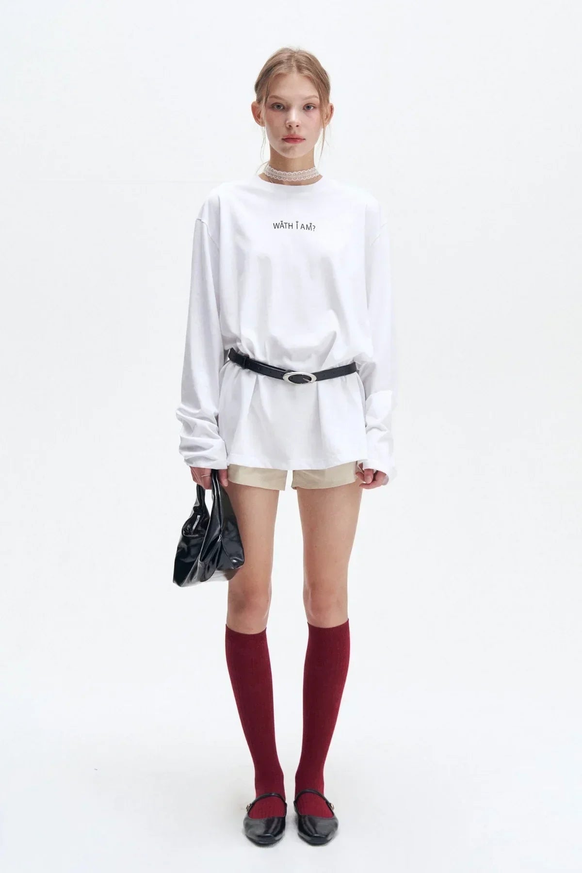 Girl wearing white long sleeve printed shirt, beige shorts, red knee socks, black belt, black shoes, holding black bag