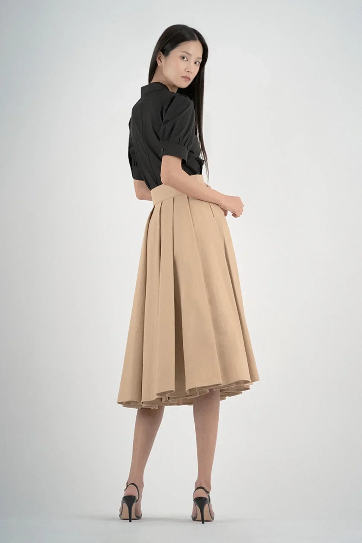 Model wearing beige pleated midi skirt with high waist and black short-sleeve blouse and black heels