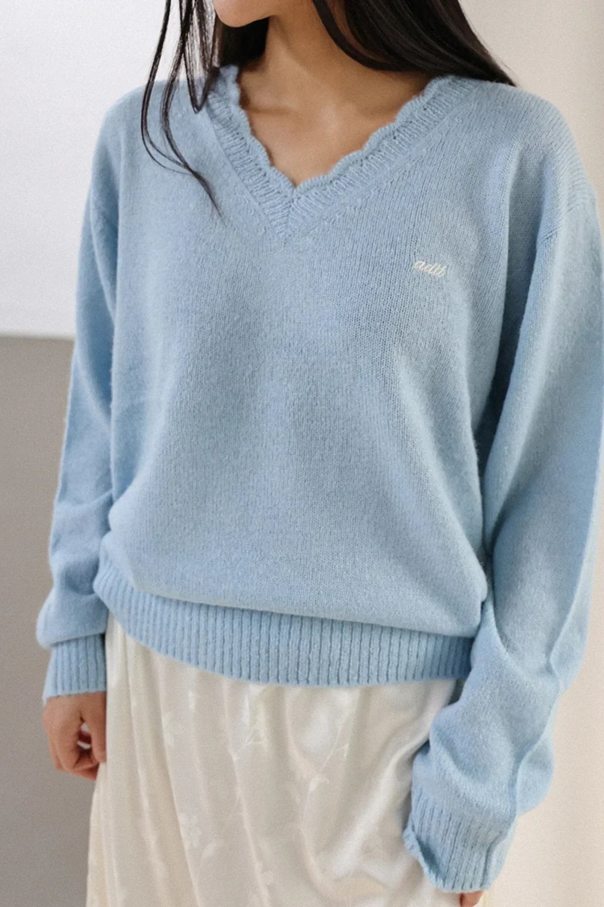 Close-up of a woman wearing a soft blue V-neck alpaca knit sweater with scalloped edges and a white skirt
