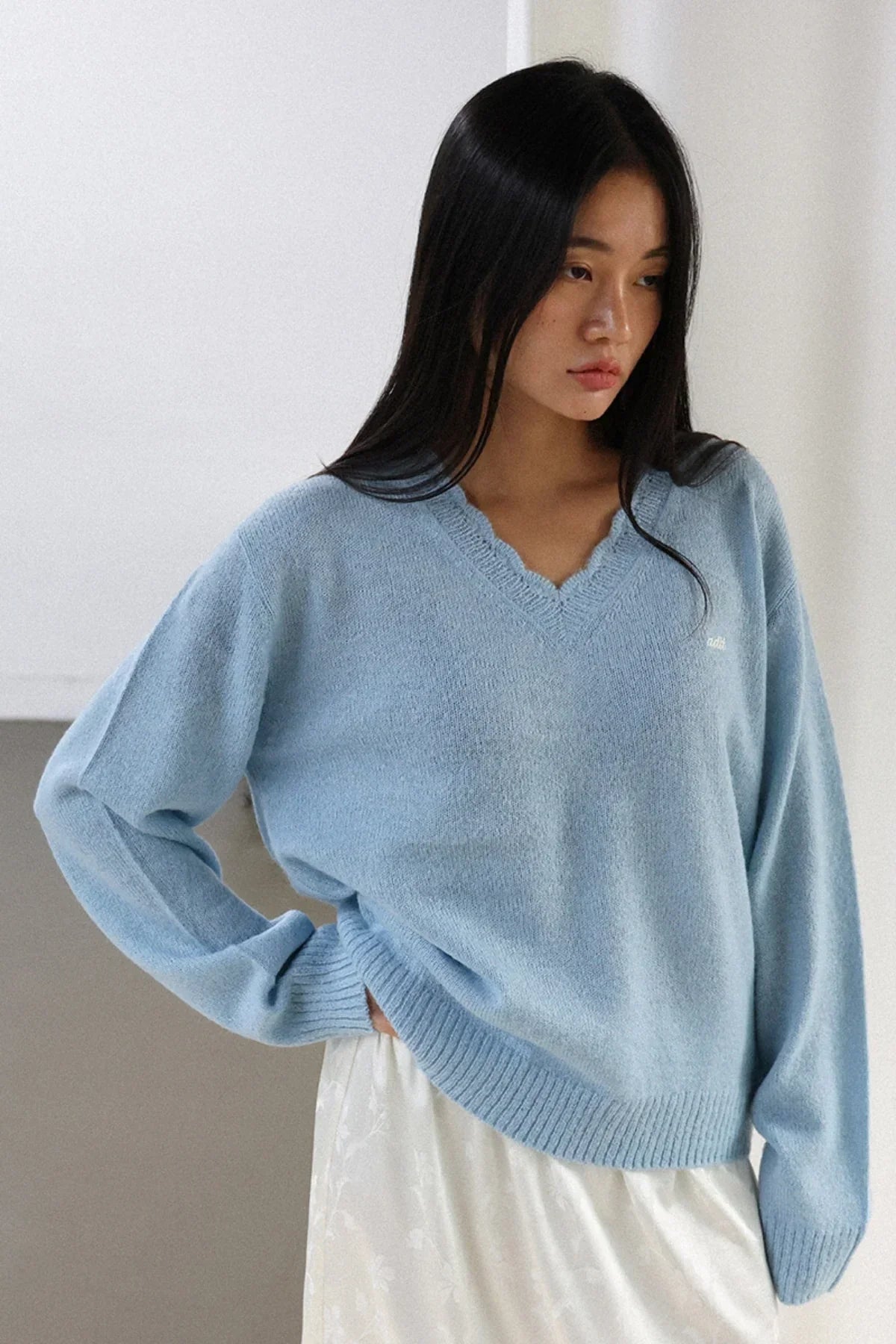 Woman wearing light blue V-neck alpaca knit sweater with scalloped edge and white skirt
