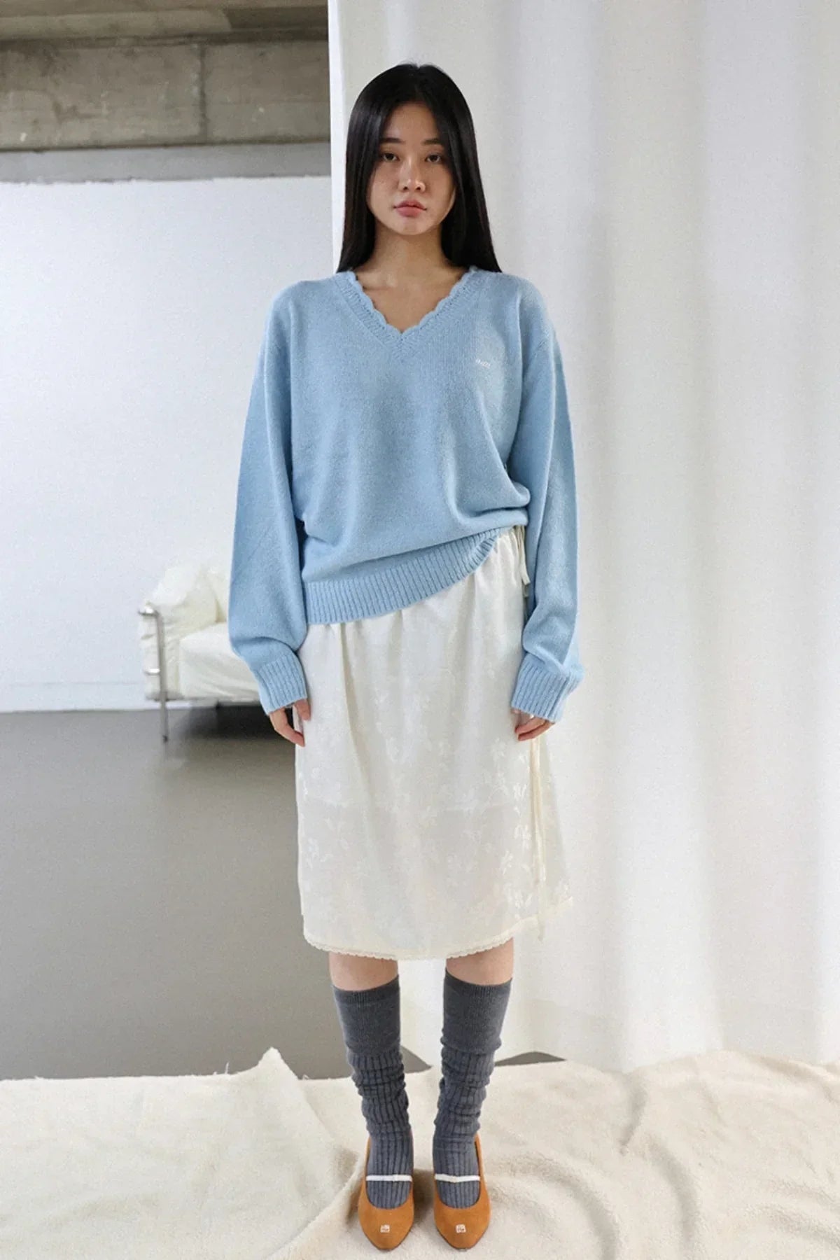 Woman wearing a light blue V-neck alpaca knit sweater with a white skirt and gray knee-high socks