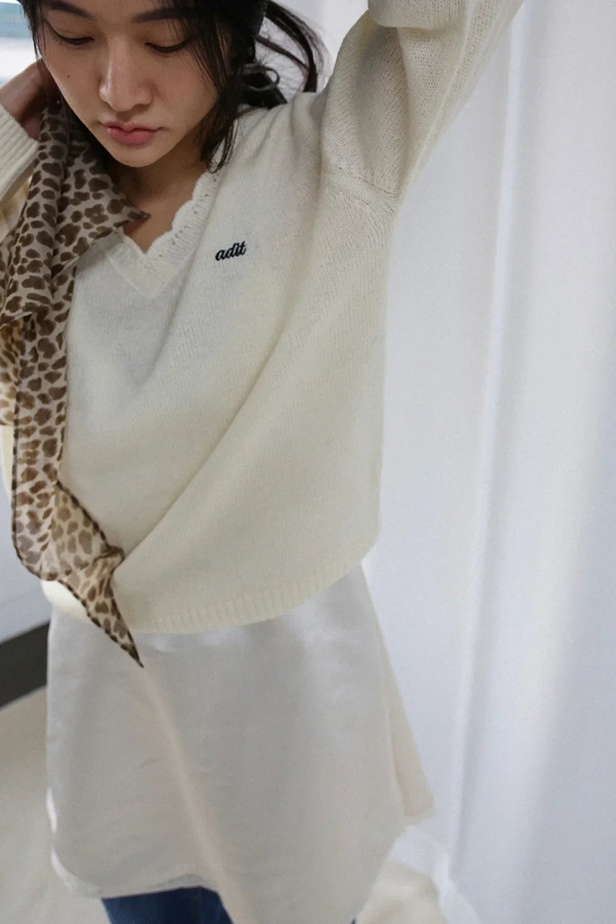 Close-up of a woman wearing an ivory wave V-neck alpaca knit sweater with leopard print scarf