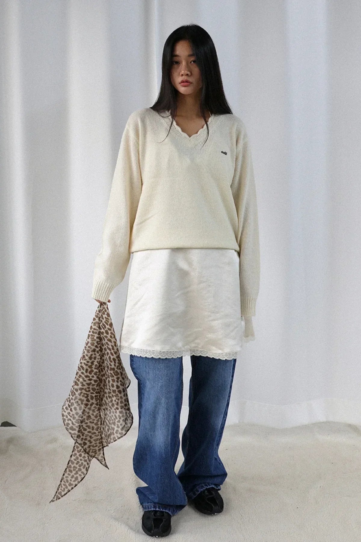 Woman wearing ivory v-neck alpaca knit sweater with lace trim skirt, blue jeans, holding leopard print scarf
