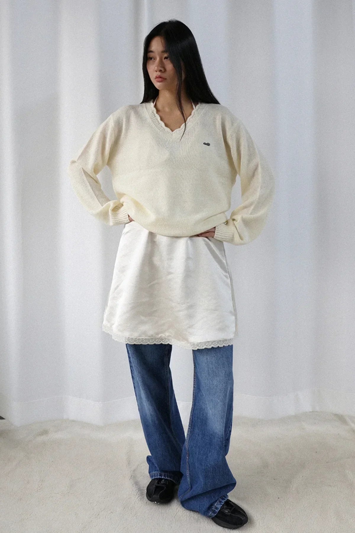 Woman wearing ivory wave V-neck alpaca knit sweater, white skirt, blue jeans, and black shoes