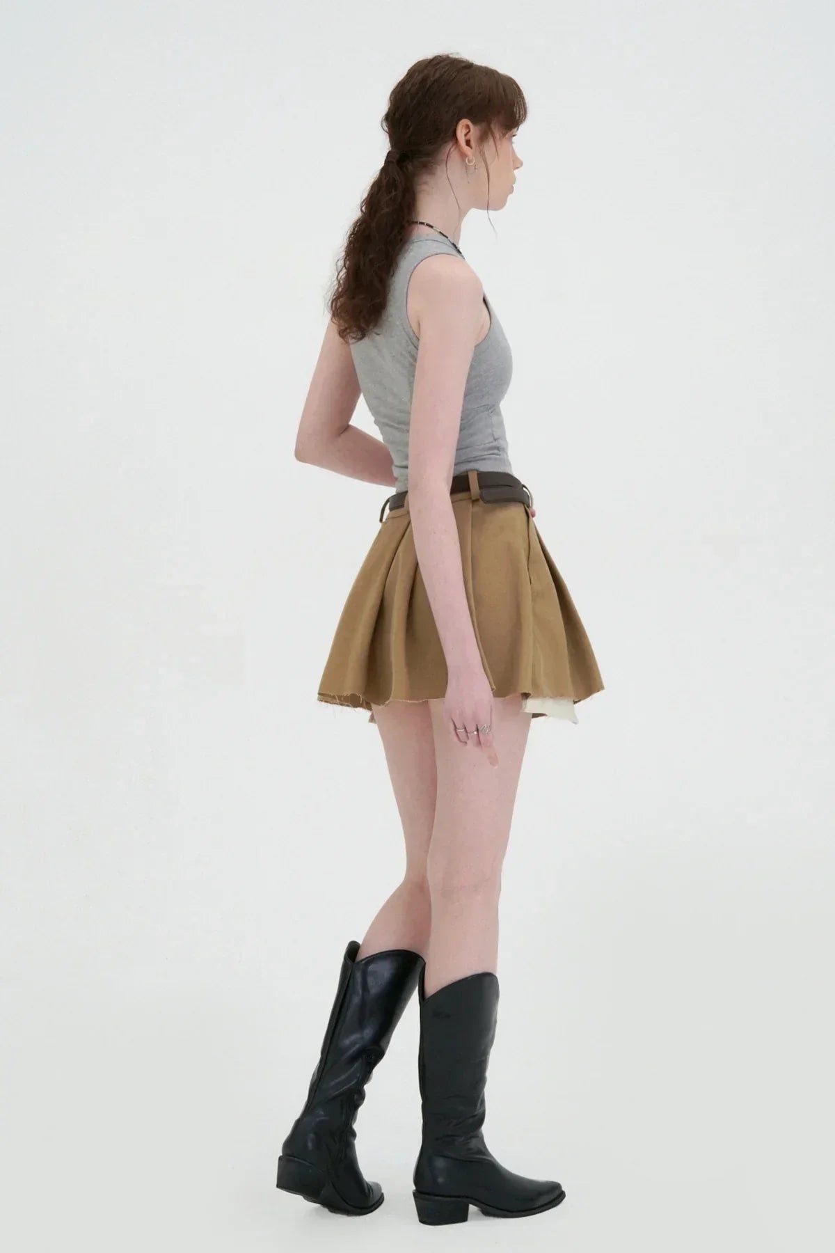 Model wearing beige wide tuck mini skirt with black belt, gray sleeveless top, and black knee-high boots