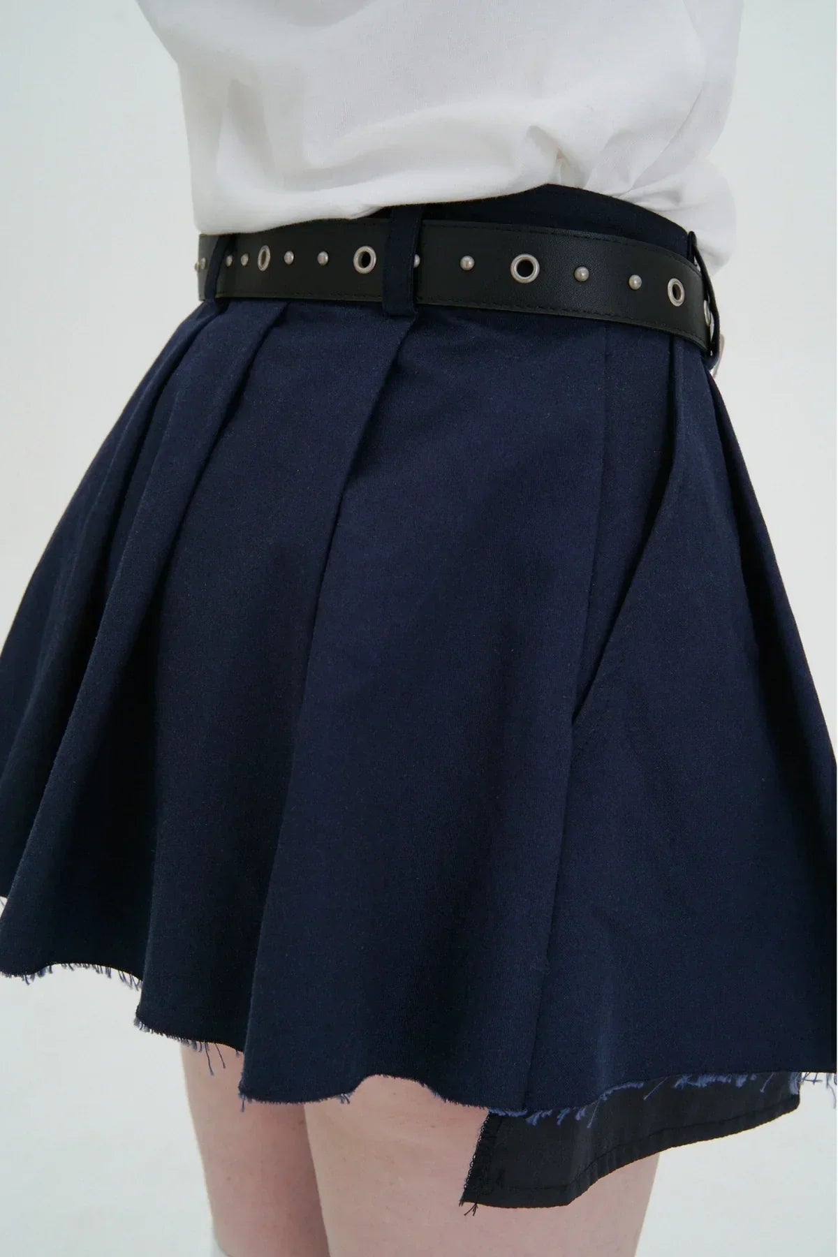 Close-up of navy blue pleated mini skirt with frayed hem and black studded belt