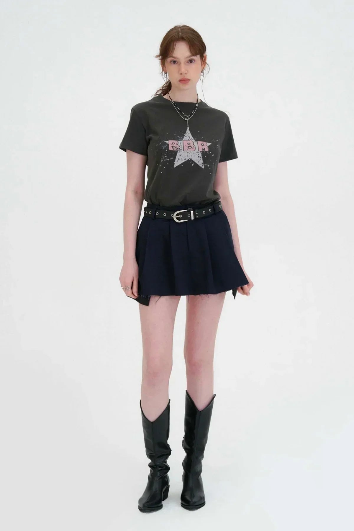 Young woman wearing black graphic tee, navy wide tuck mini skirt with belt, and black knee-high boots