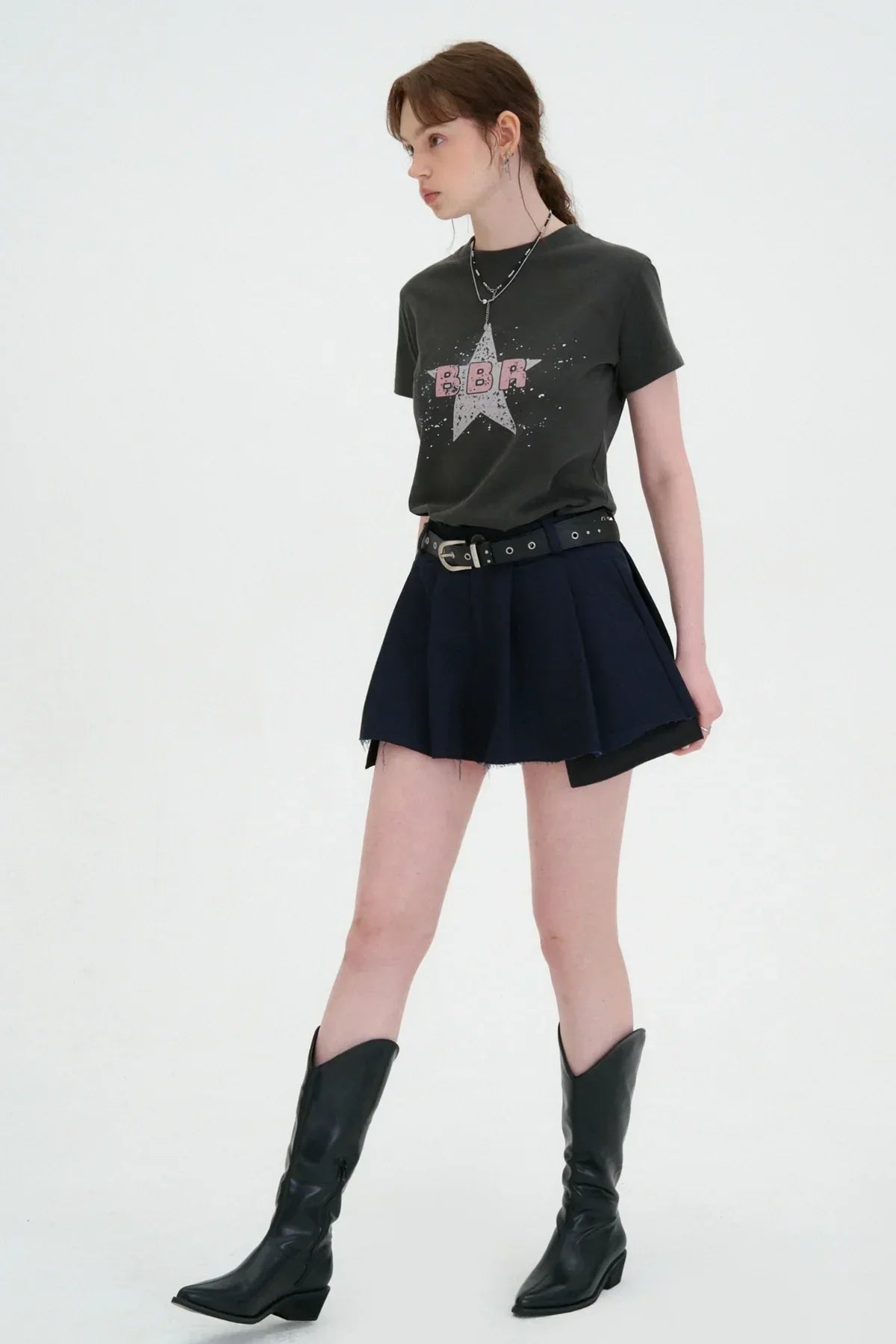 Woman wearing a black graphic t-shirt and navy wide tuck mini skirt with black belt and black boots