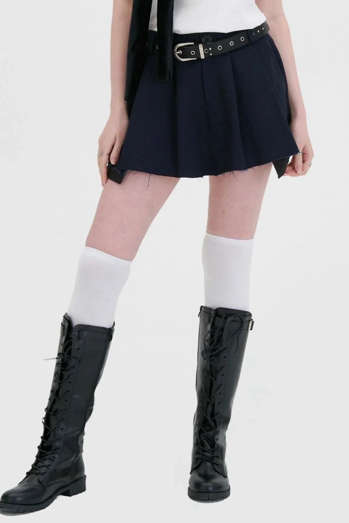 Woman wearing navy wide tuck mini skirt with black belt, white knee socks, and black lace-up boots