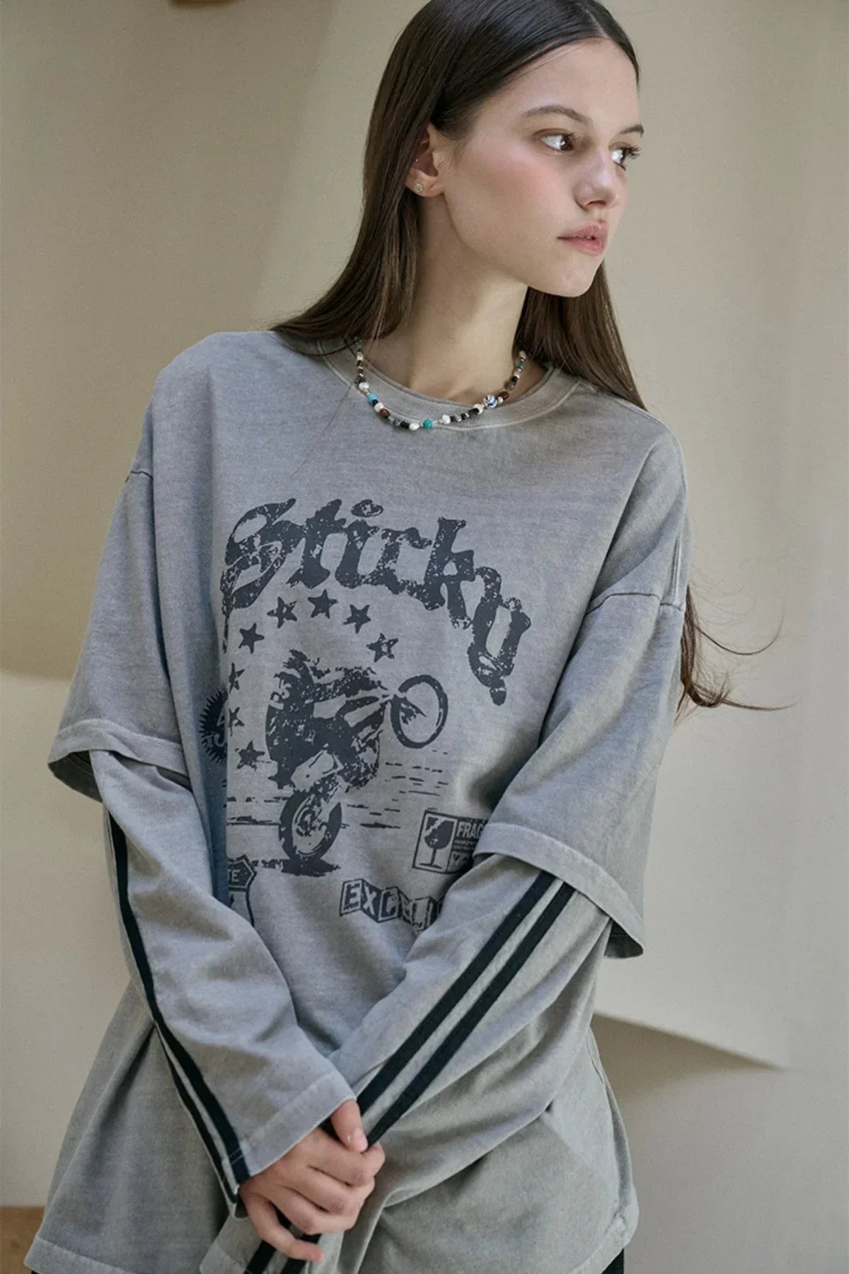 Young woman wearing layered gray long sleeve and graphic t-shirt with motorbike print indoors
