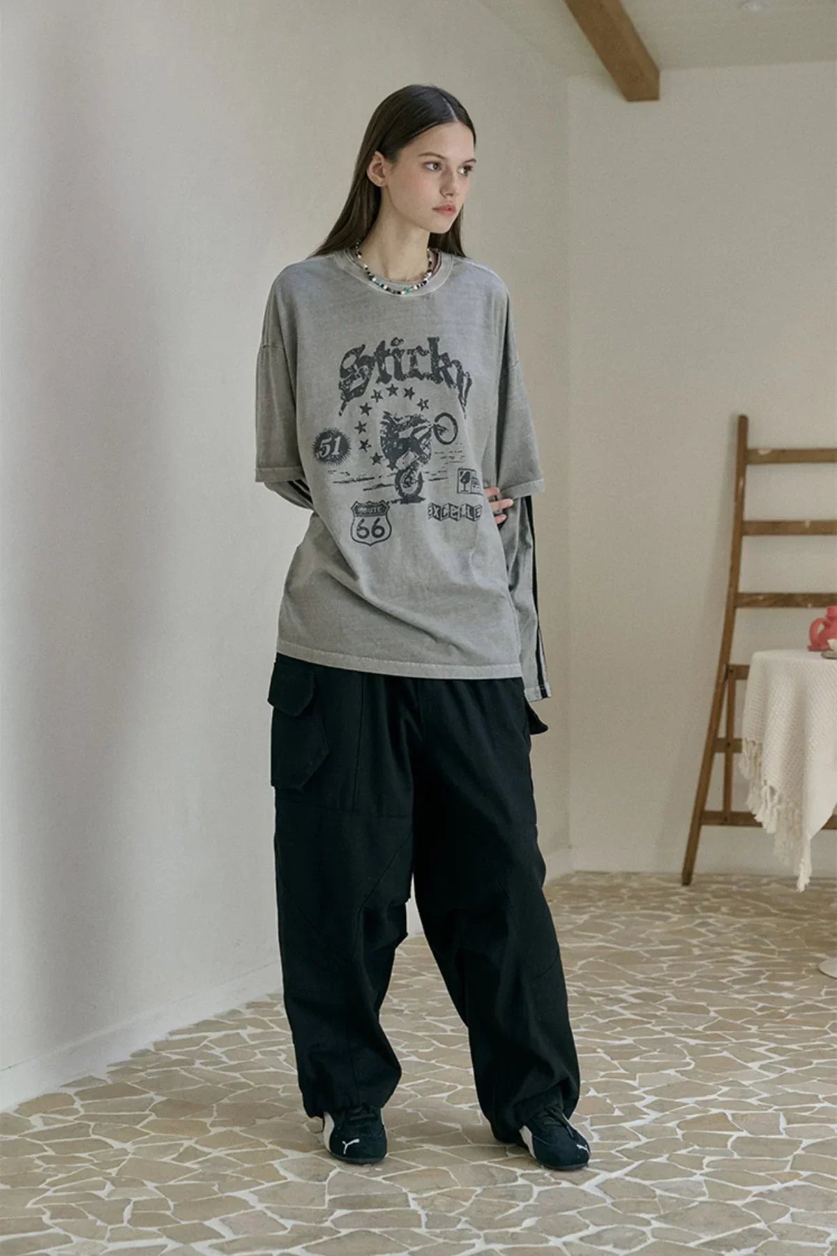 Model wearing ghost gray graphic oversized T-shirt with black cargo pants and sneakers in minimalist room