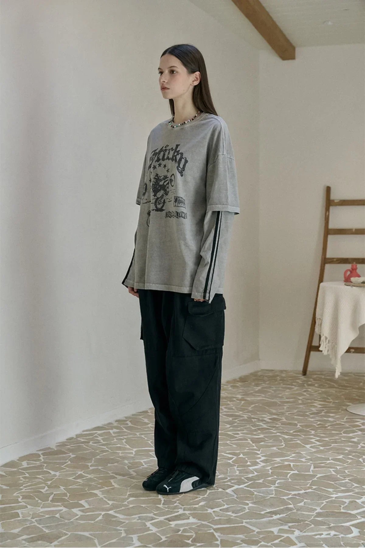 Young woman modeling ghost gray layered long-sleeve shirt with graphic print and black cargo pants indoors