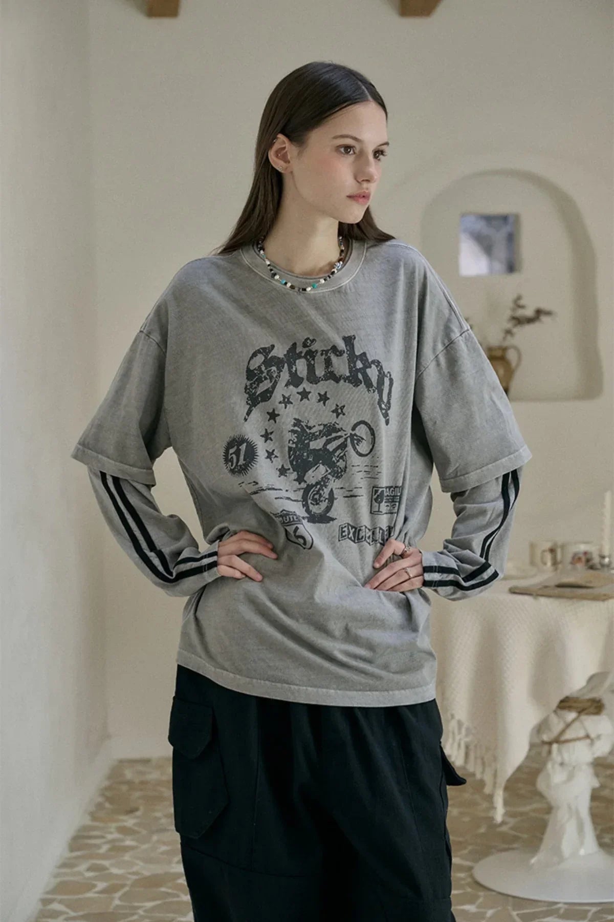 Young woman wearing layered long-sleeve ghost gray graphic T-shirt with black cargo pants in minimalist room