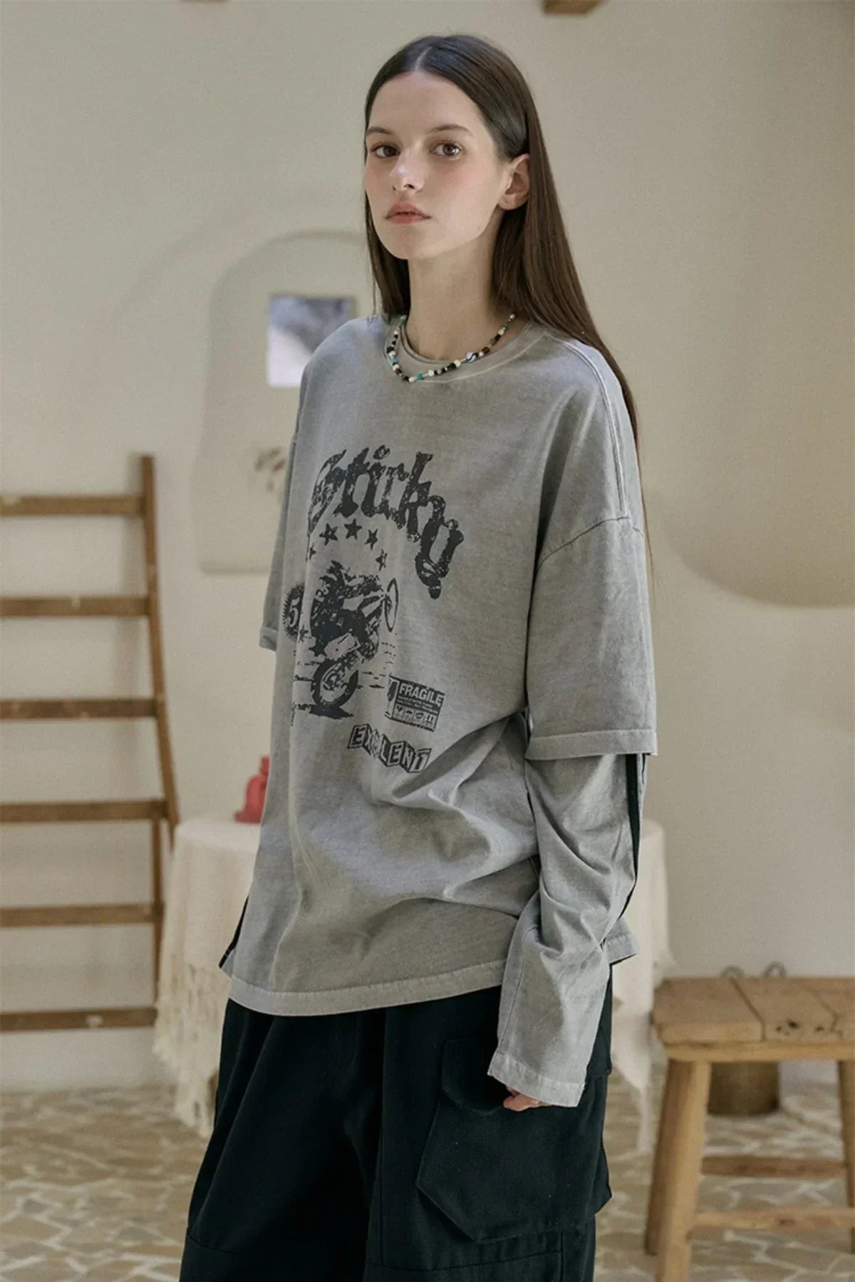 Young woman wearing ghost gray layered long-sleeve graphic tee and black cargo pants indoors