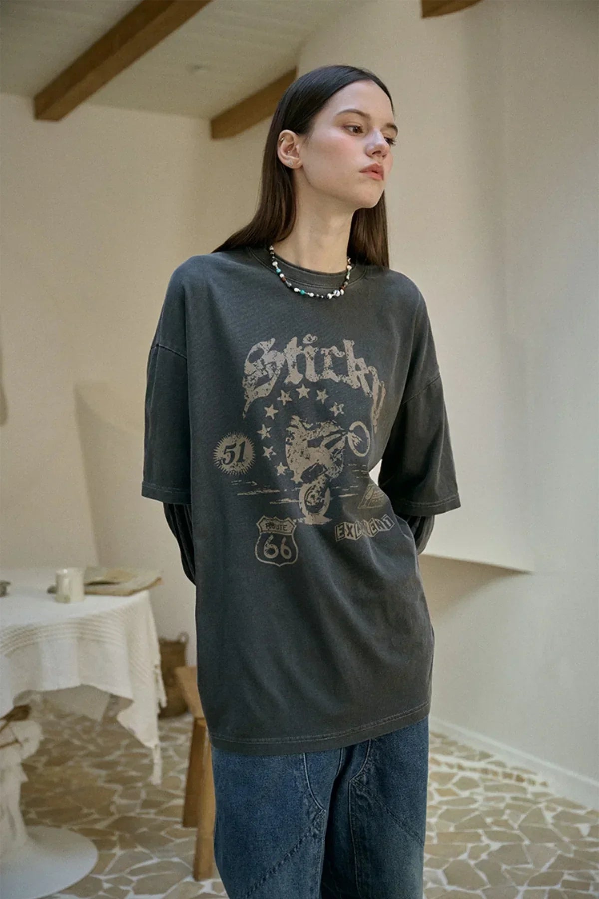 Woman wearing smoke black vintage-style graphic oversized T-shirt in minimal indoor setting with tiled floor