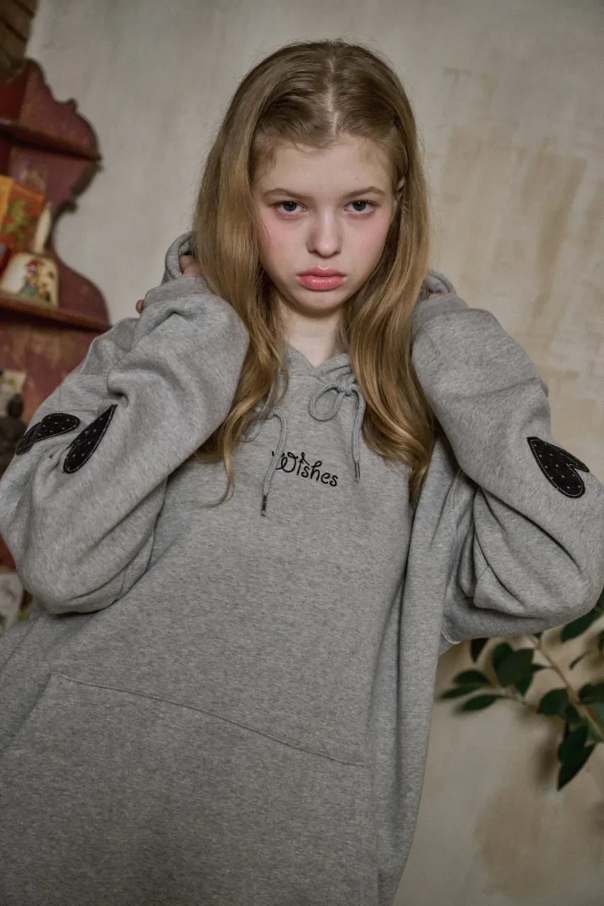 Young woman wearing gray hoodie with black heart patches on sleeves and 'Wishes' text