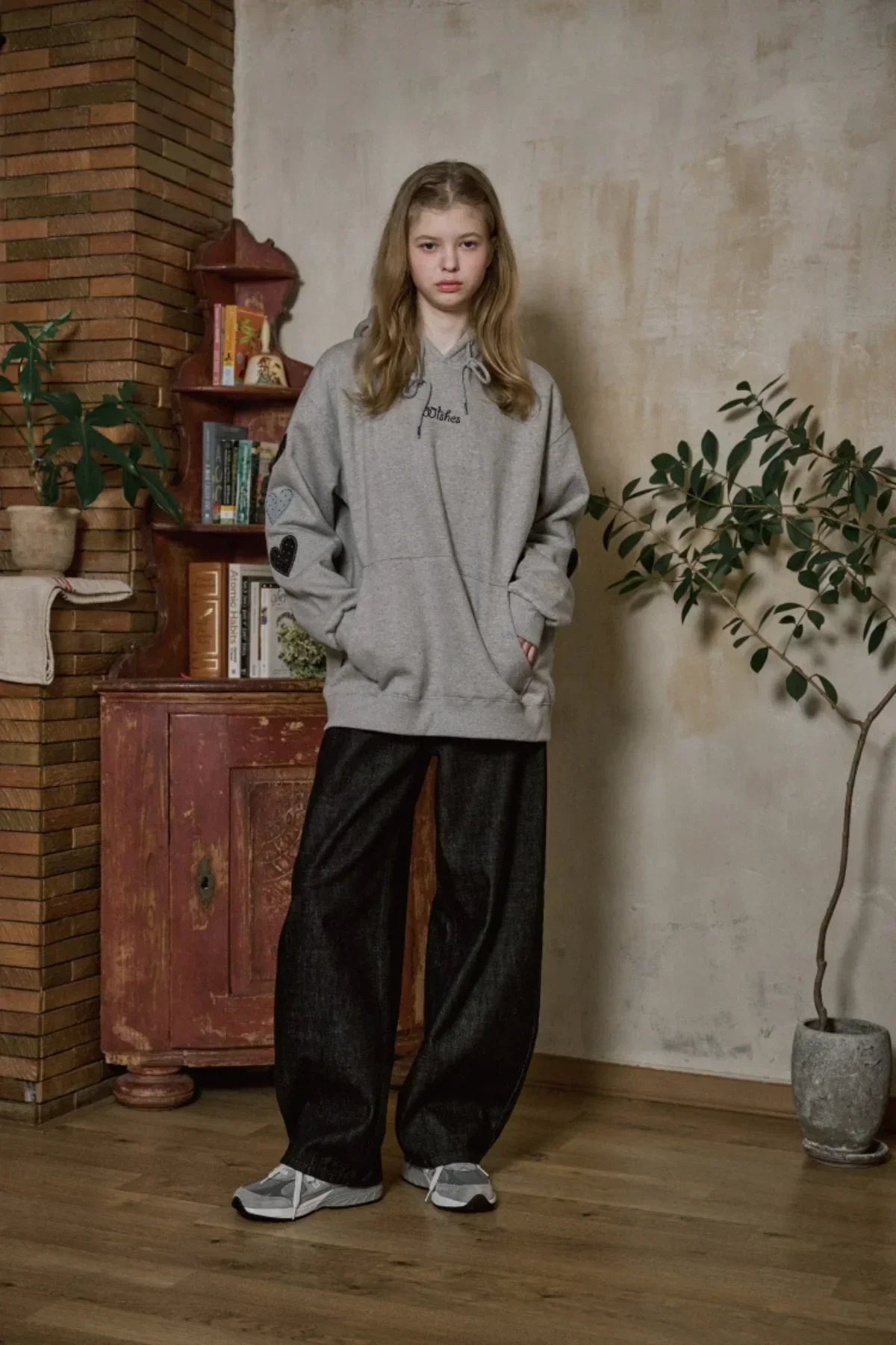 Young woman wearing gray hoodie with heart patches and black wide-leg pants in vintage room