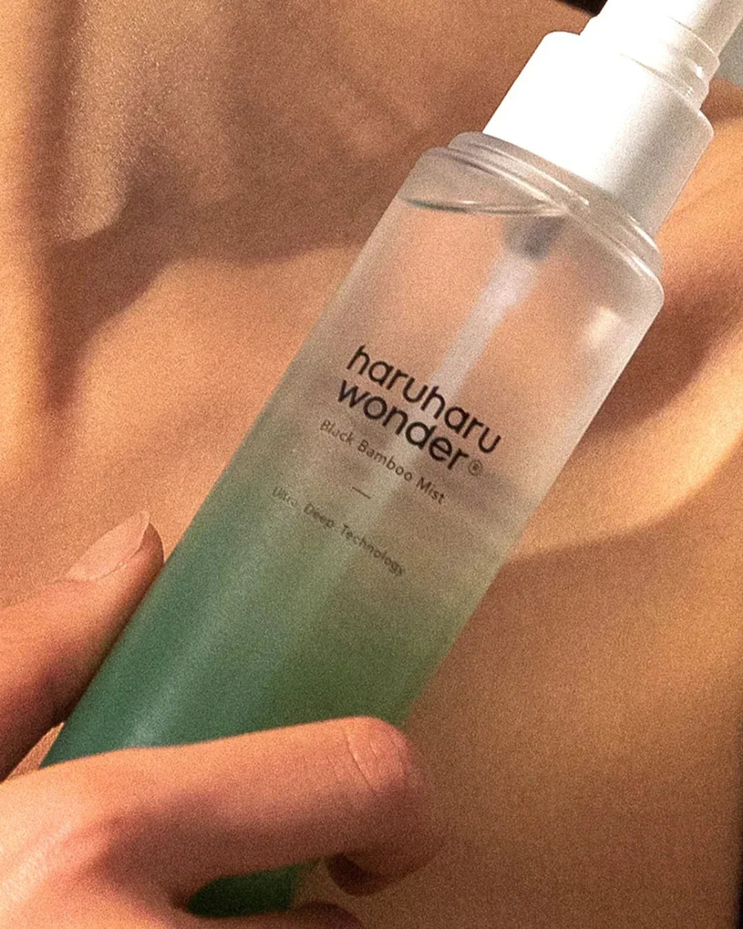 Hand holding Haruharu Wonder Black Bamboo Mist bottle with green liquid against skin background