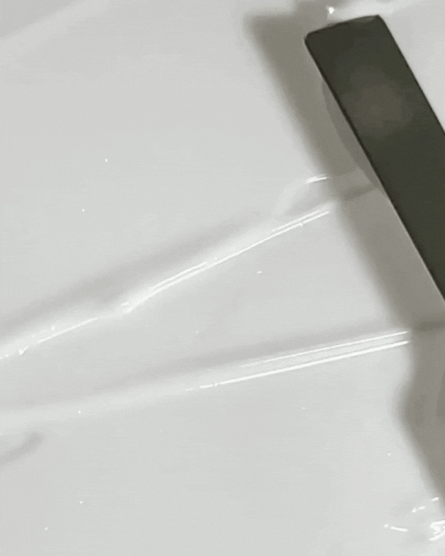 Close-up of clear, glossy skincare cream texture on white surface with a black spatula spreading it