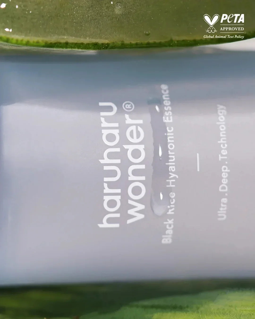 Close-up of Haruharu Wonder Black Rice Hyaluronic Essence bottle with water droplets and PETA approval logo
