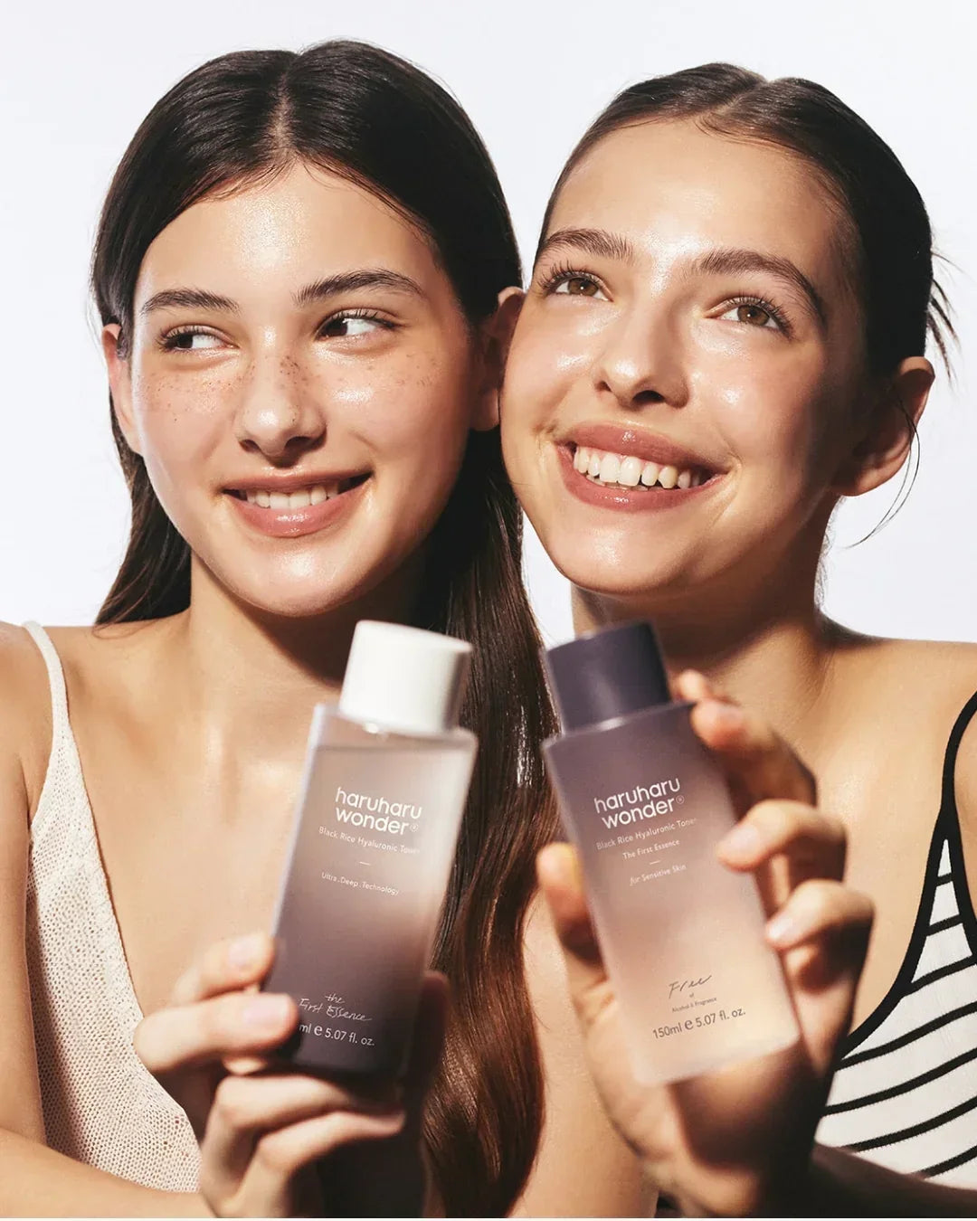 Two smiling women holding Haruharu Wonder Black Rice Hyaluronic Toner skincare bottles