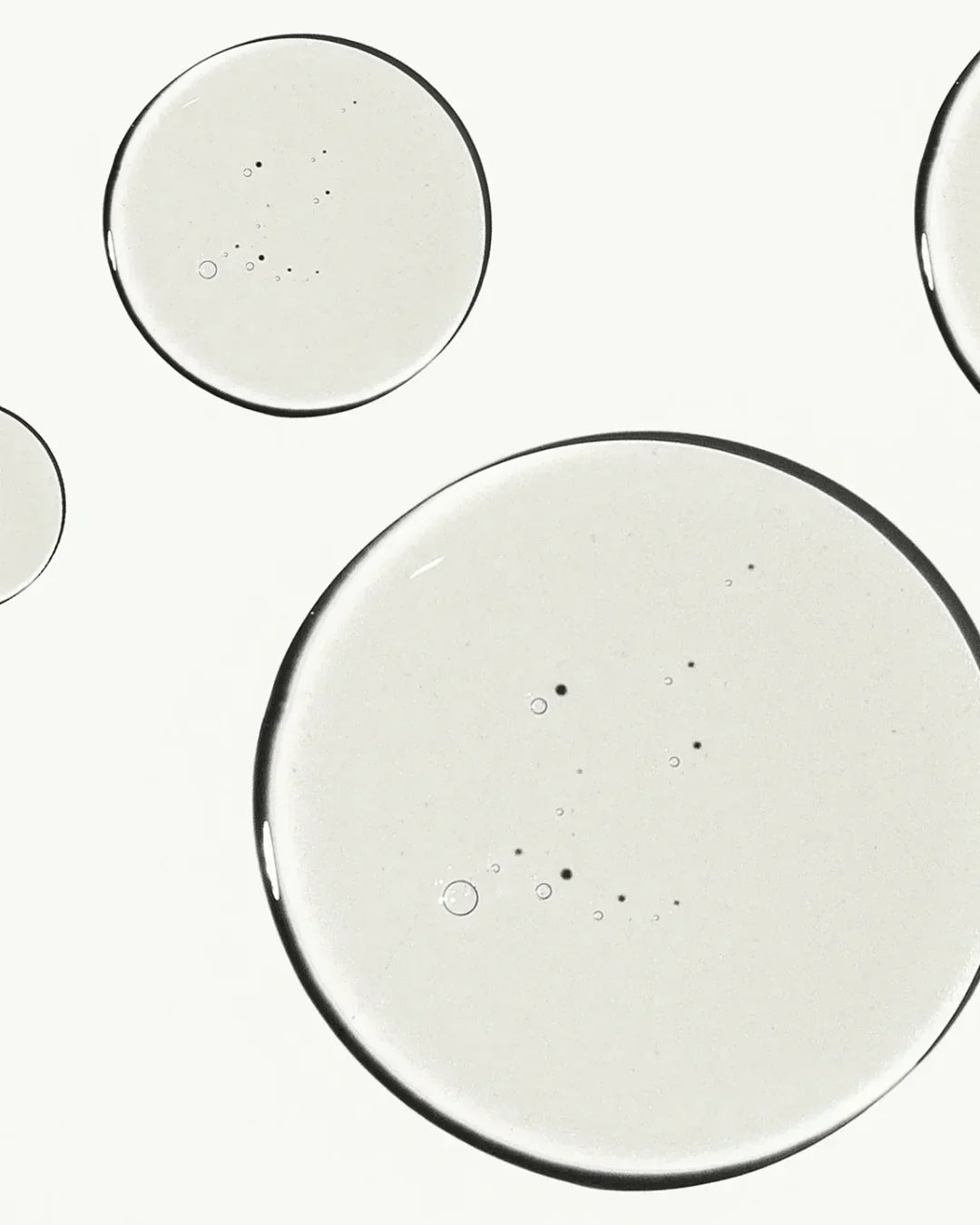 Close-up of clear liquid drops with small air bubbles on white background, showing texture