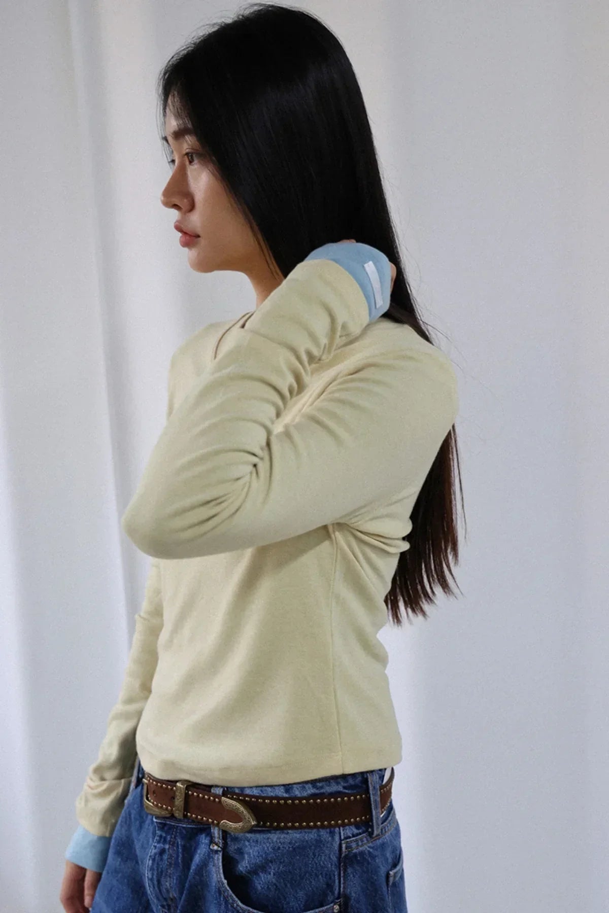Side view of woman wearing light yellow wool v-neck long sleeve tee with blue cuffs and jeans
