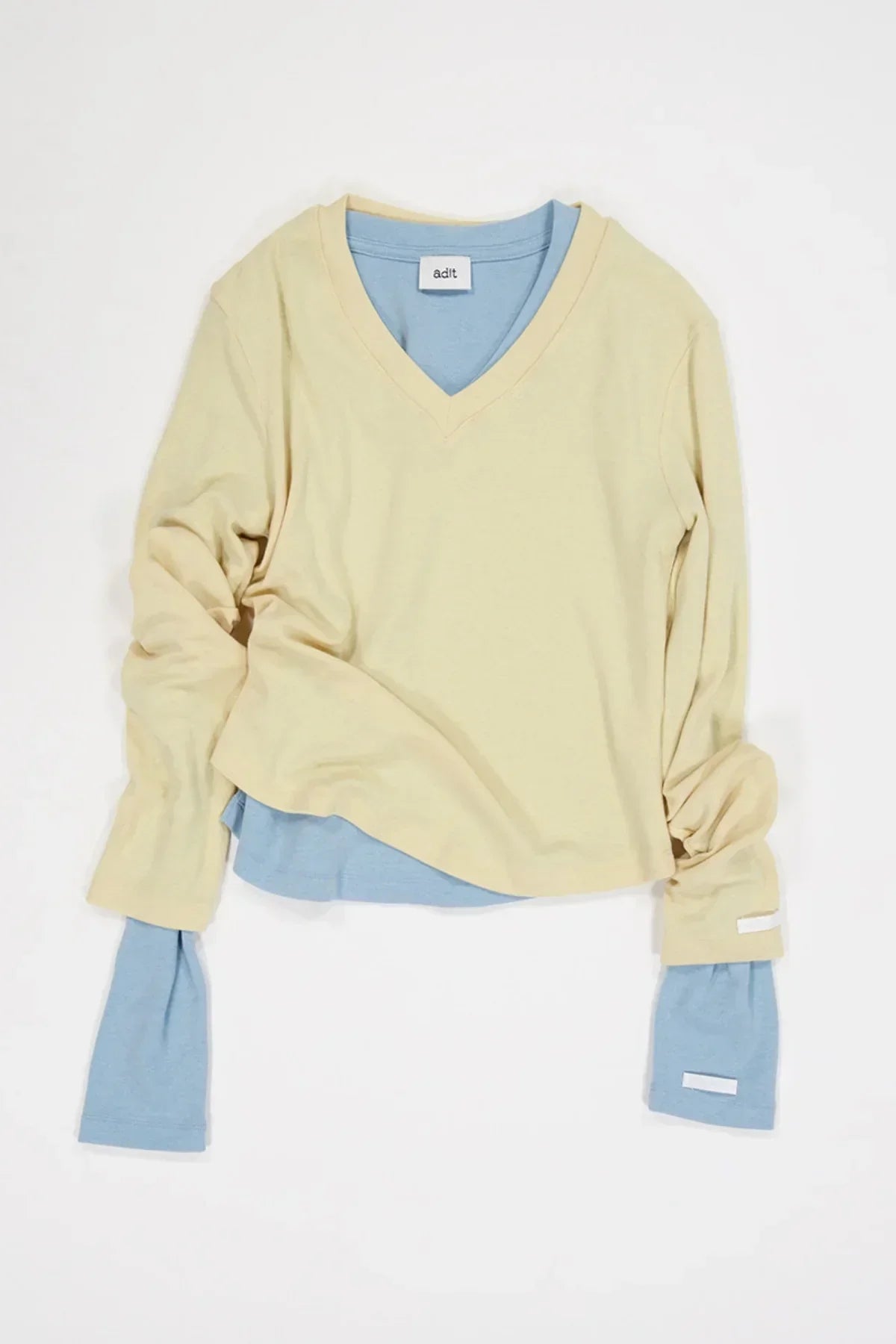 Layered long sleeve V-neck shirts in pale yellow and light blue on white background