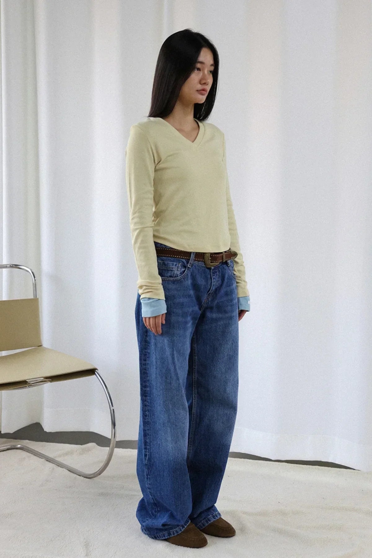 Young woman wearing lime v-neck long sleeve shirt with layered cuffs, loose blue jeans, brown belt, and brown shoes