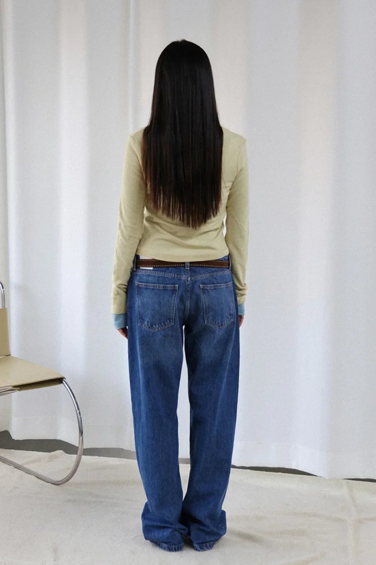 Rear view of woman with long straight hair wearing lime V-neck wool long-sleeve tee and loose blue jeans