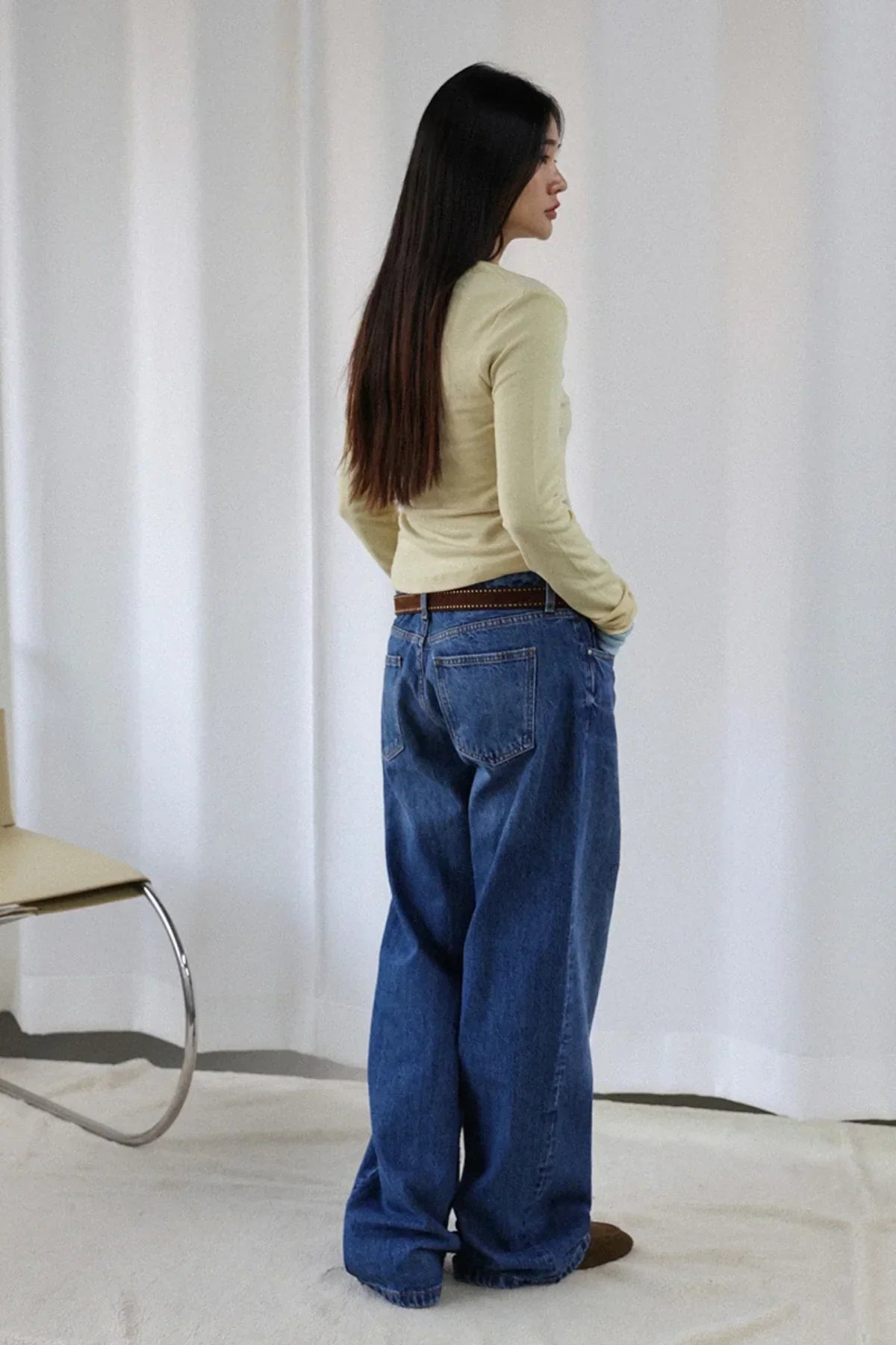 Woman with long black hair wearing lime wool V-neck long sleeve tee and baggy blue jeans in studio
