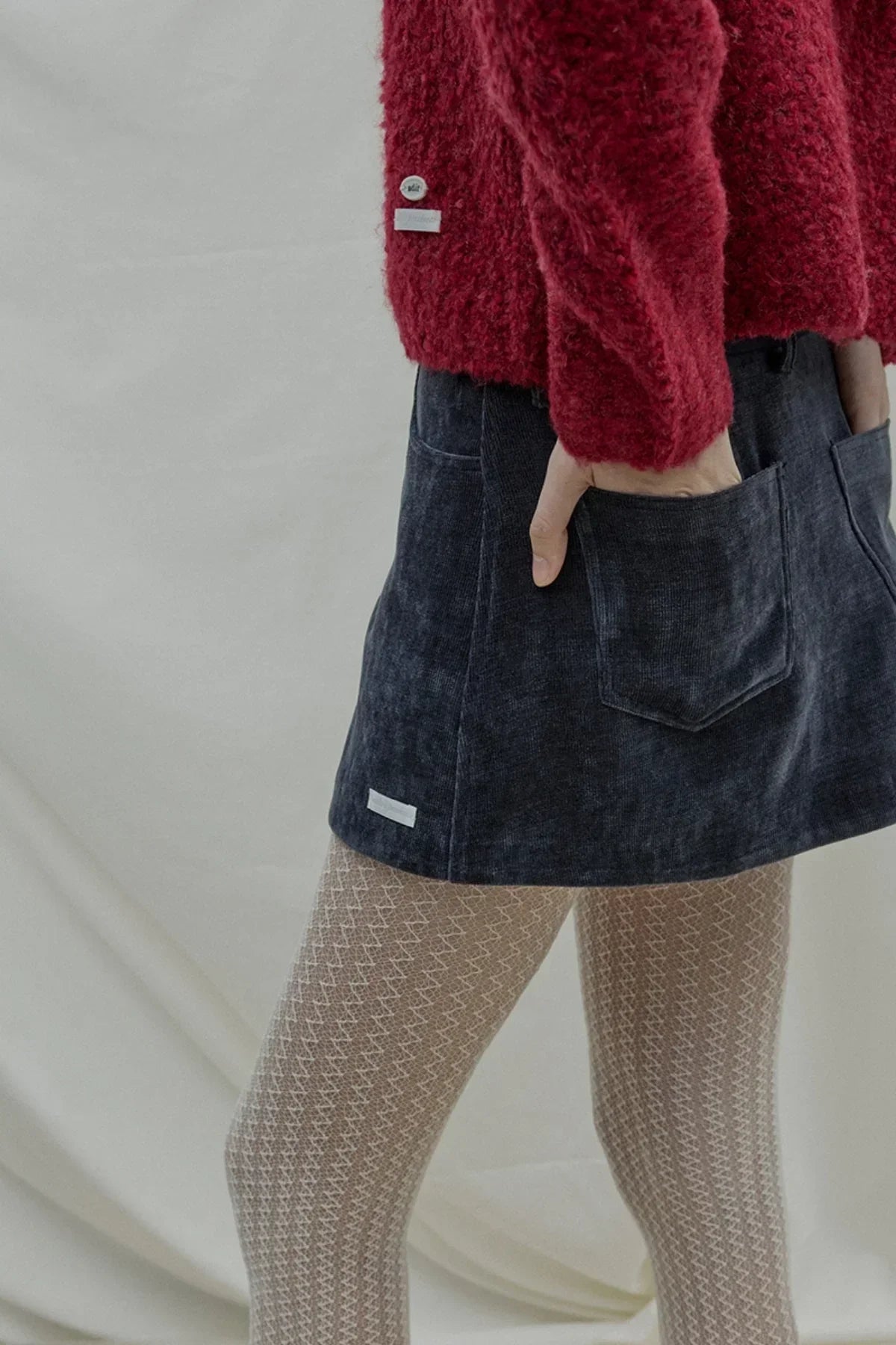 Close-up of a navy wrap skirt with pockets worn with beige patterned tights and a red fuzzy sweater