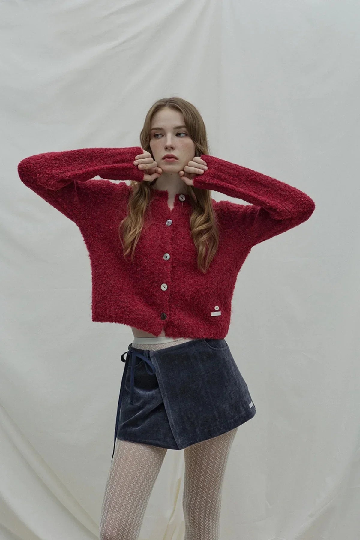 Young woman wearing fuzzy red button-up sweater and navy blue wrap skirt with white patterned tights