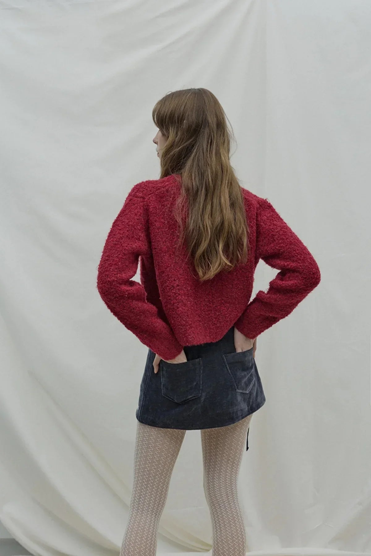 Woman wearing red fuzzy sweater, navy corduroy skirt with back pockets, and patterned white tights