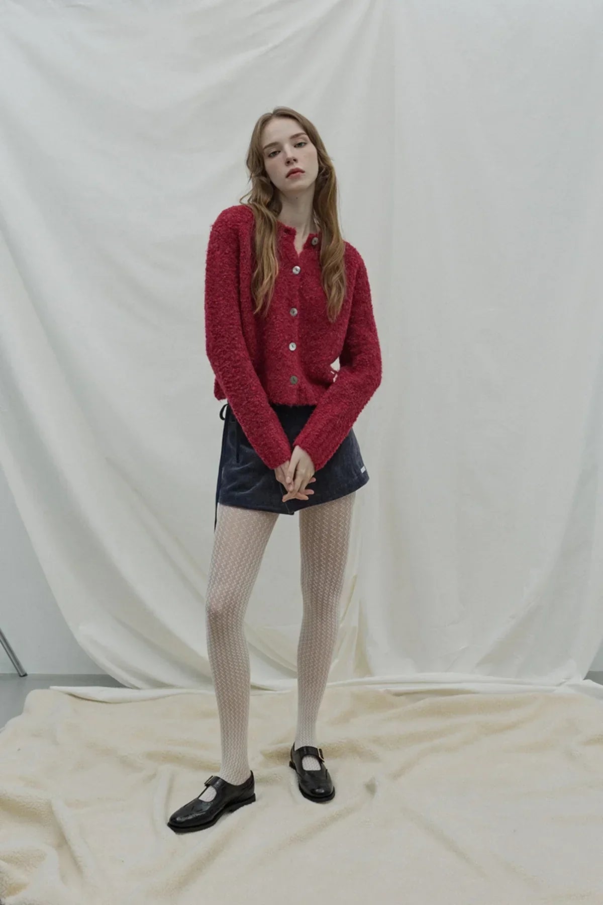 Model wearing red fuzzy button-up cardigan with navy wrap skirt, patterned tights, and black Mary Jane shoes