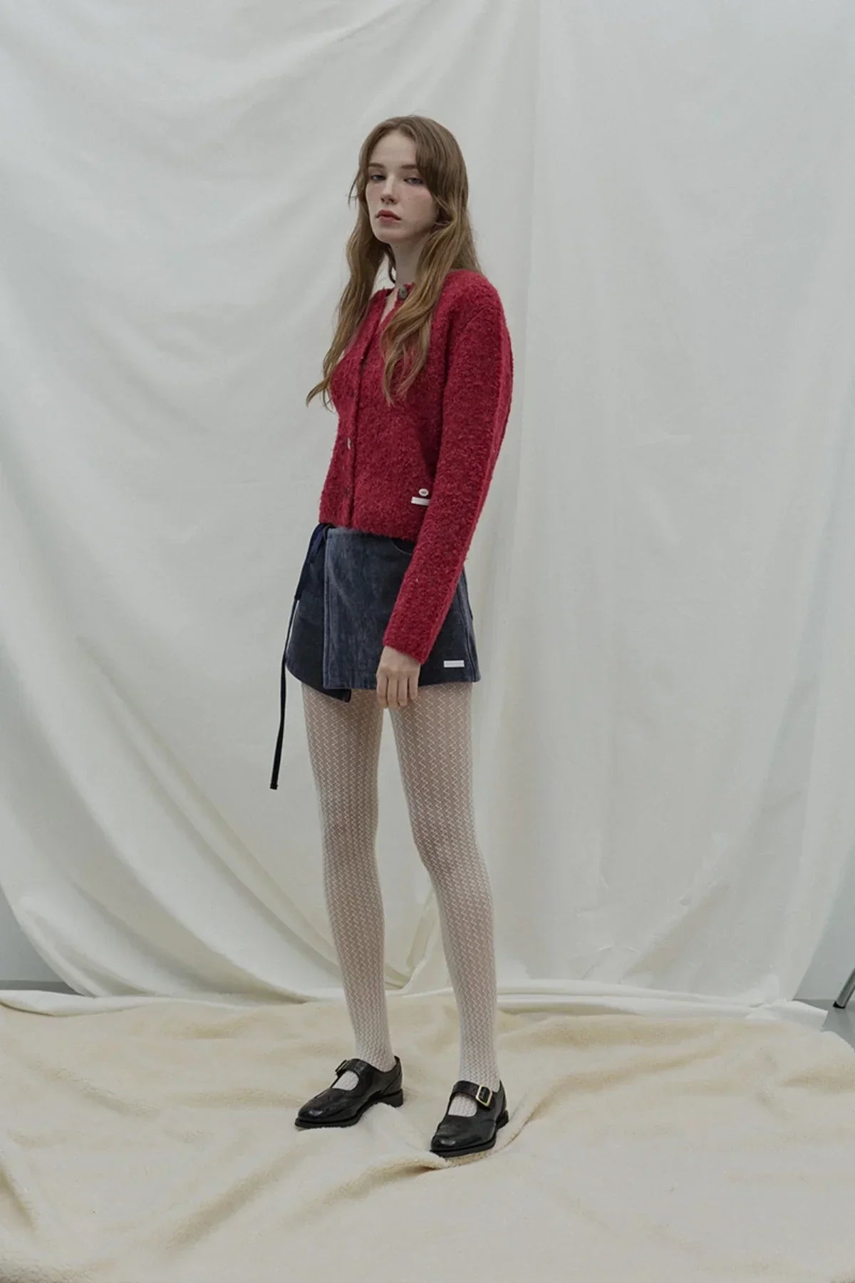 Model wearing red fuzzy cardigan, navy blue wrap mini skirt, patterned white tights, and black buckle shoes