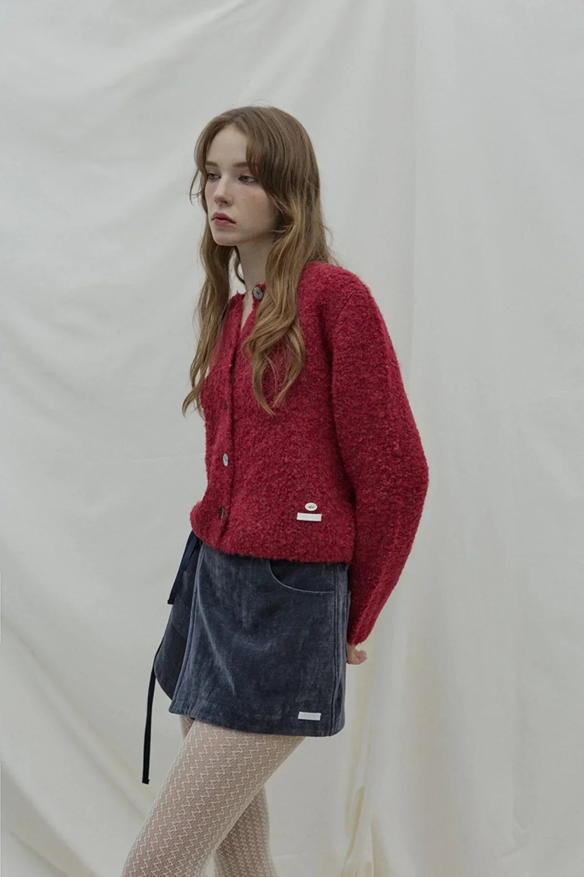 Model wearing red textured cardigan and navy blue velvet wrap skirt with patterned tights in studio