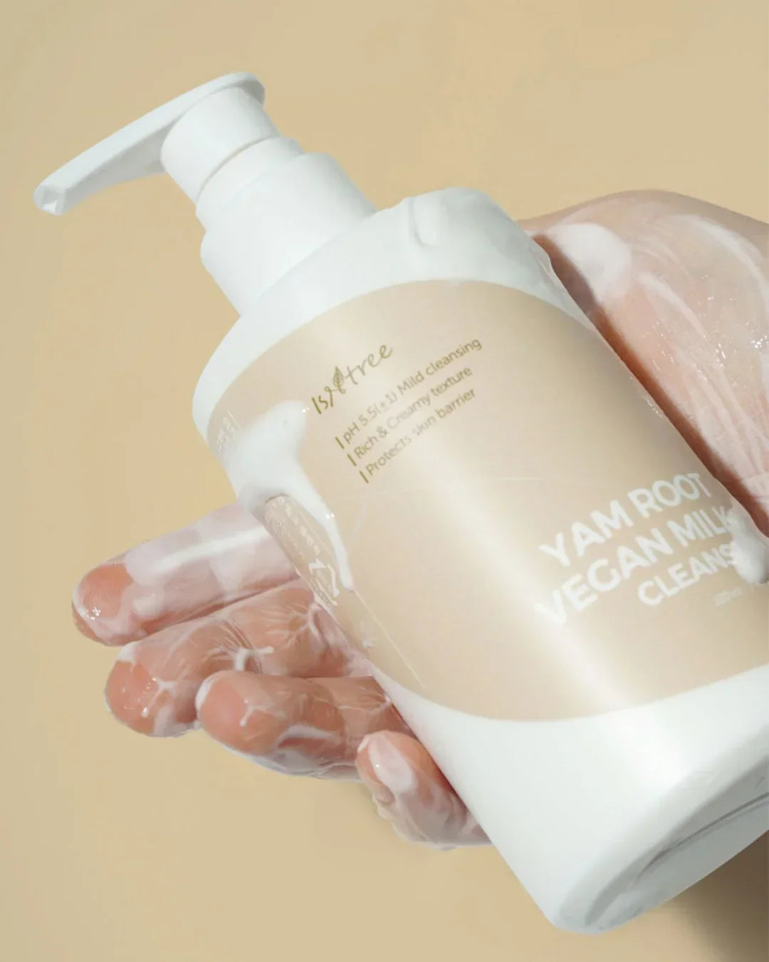 Hand covered in creamy cleanser holding a pump bottle of Isntree Yam Root Vegan Milk Cleanser